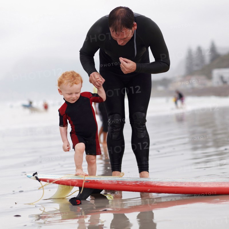 Father and his son (2-3) on beach by surfboard