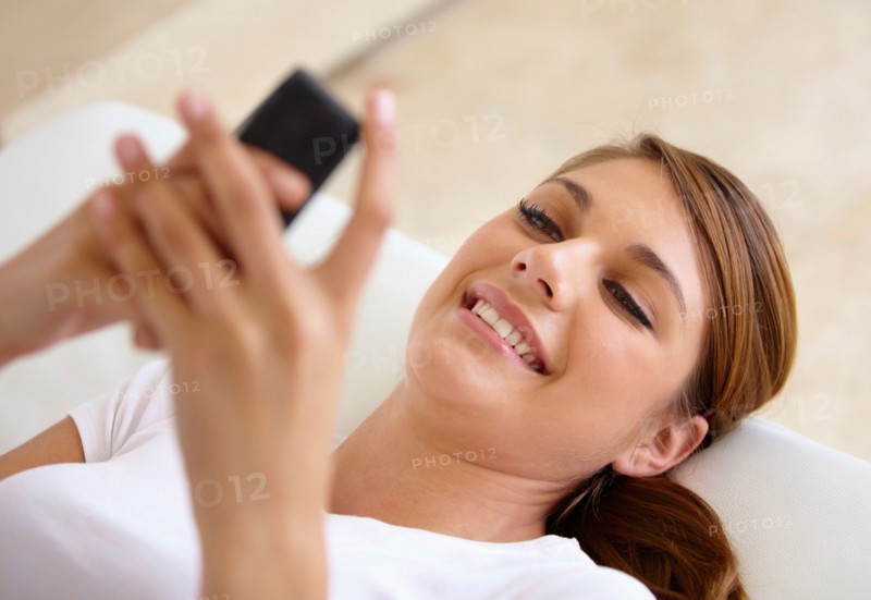 Young woman lying on bed and using cell phone