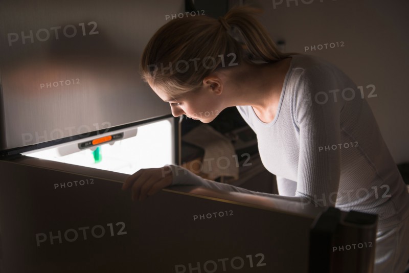 Woman opening fridge at night.