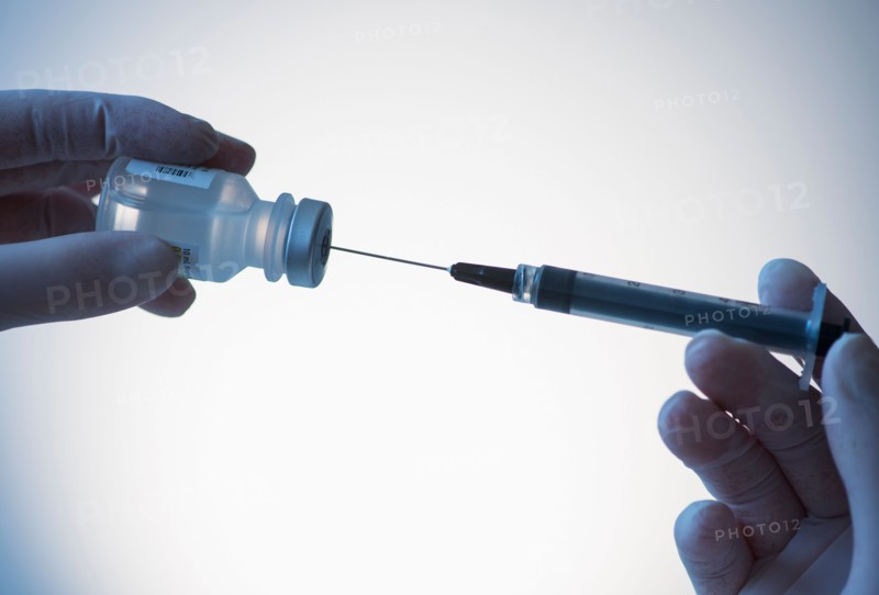 Close up of hands in surgical gloves preparing syringe for injection, studio shot.