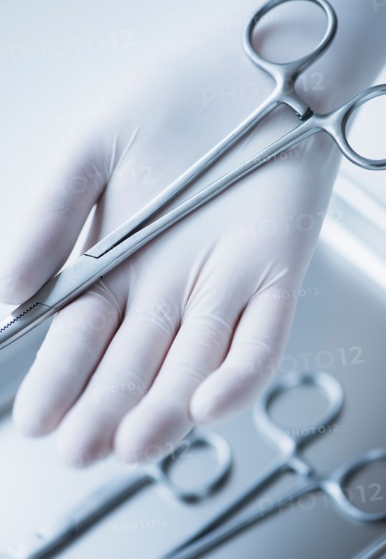 Close up of hand in surgical glove holding dental forceps, studio shot.