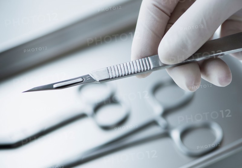 Close up of hand in surgical glove holding dental scalpel, studio shot.