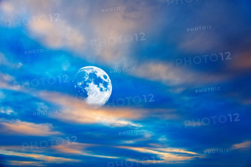 Moon behind clouds at dusk.