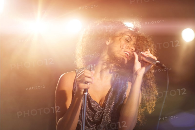 Young woman singing in spotlight.