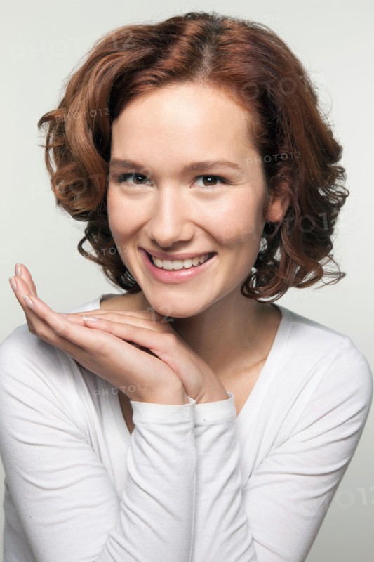 Studio shot portrait of young woman in white blouse with hands clasped
