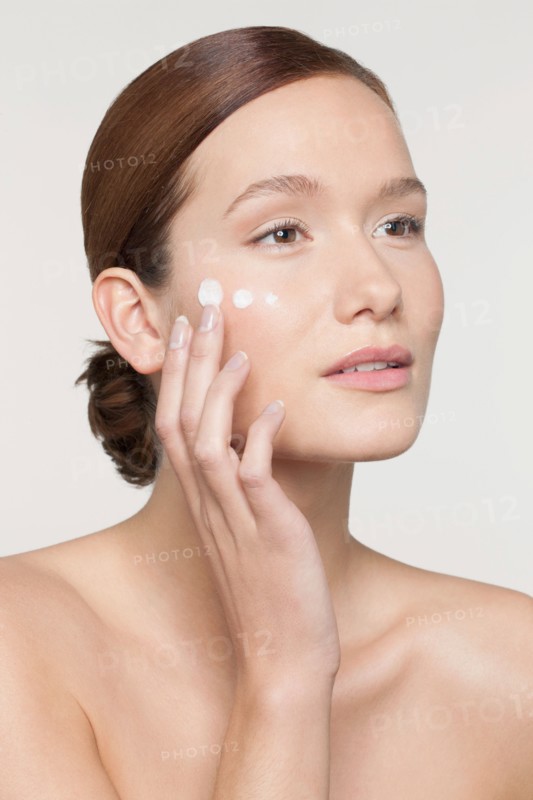 Studio shot of young woman applying moisturizer on face