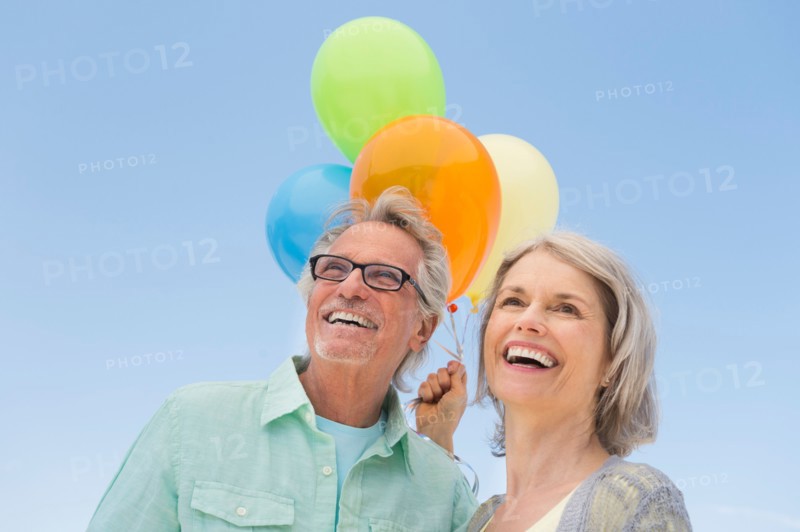 Senior couple with bunch of balloons against clear sky.