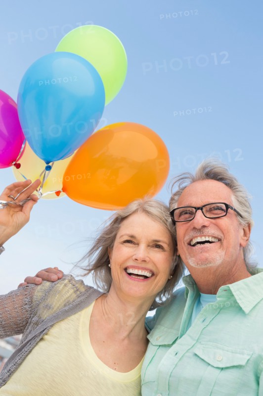 Senior couple with bunch of balloons against clear sky.
