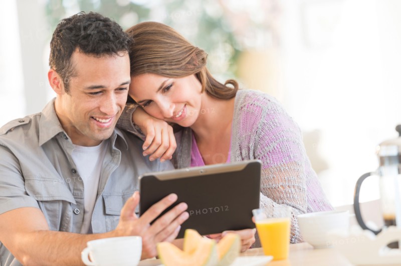 Young couple using digital tablet at kitchen table.