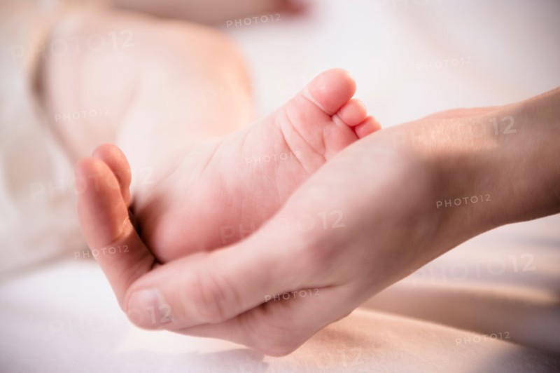 Close up of mother's hand holding tiny foot of baby girl (6-11 months)