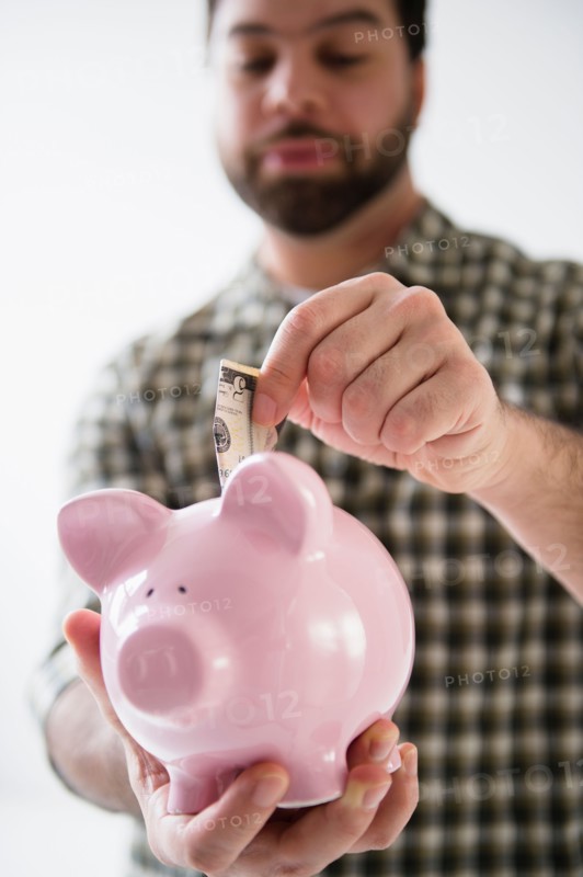 Portrait of man holding piggy ban and putting money inside