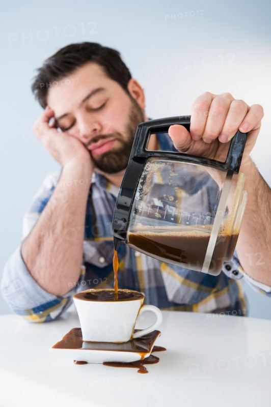 Tired, sleepy man spilling coffee on table