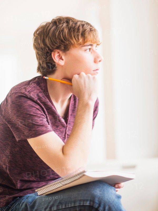 Teenage boy (14-15) sitting and holding pencil and note pad
