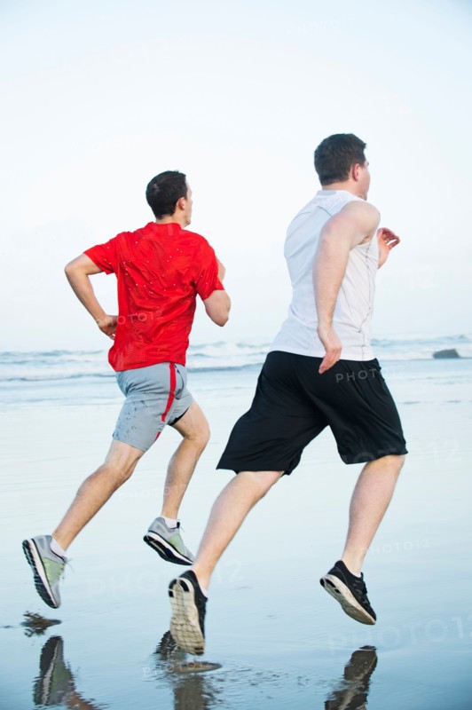 Young adult men running on beach