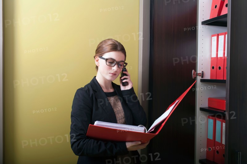 Businesswoman reading files and talking on cell phone