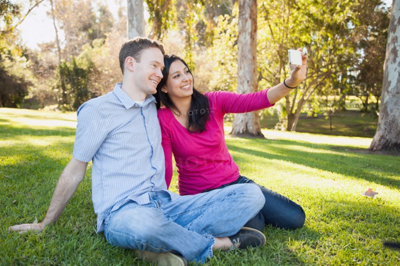 Couple sitting on grass in park photographing themselves