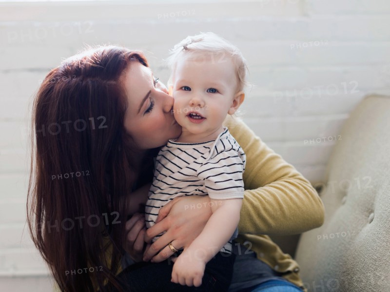 Portrait of mother sitting on sofa and kissing her daughter (12-17 months)
