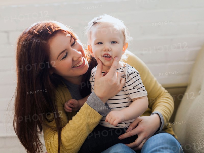 Portrait of mother sitting on sofa and touching face of her daughter's (12-17 months)