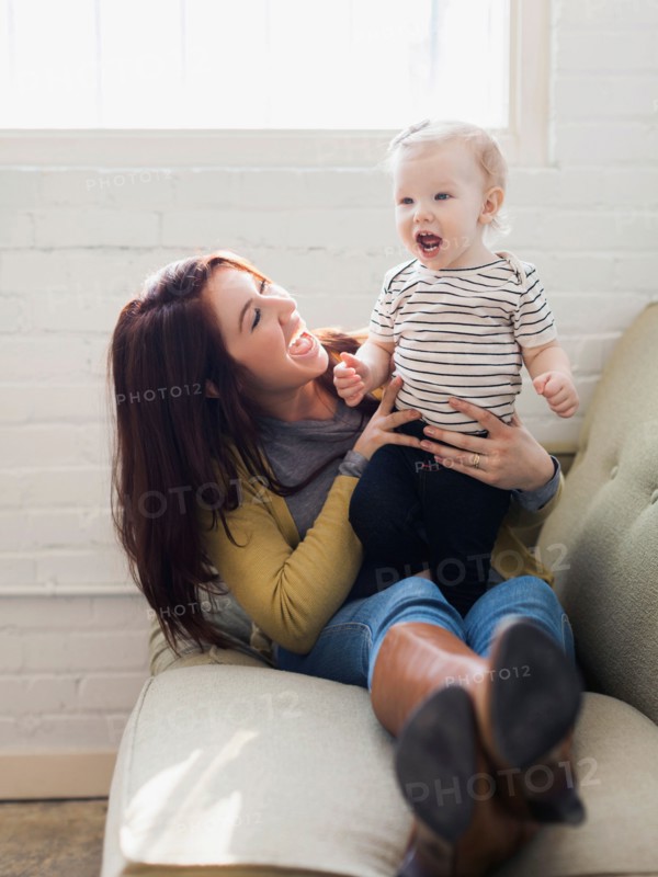 Mother and daughter (12-17 months) playing on sofa, Laughing and having fun