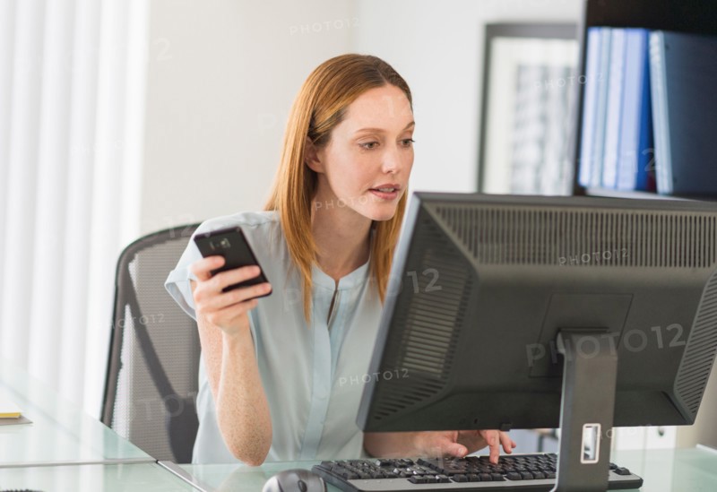 Business woman using computer and phone in office.