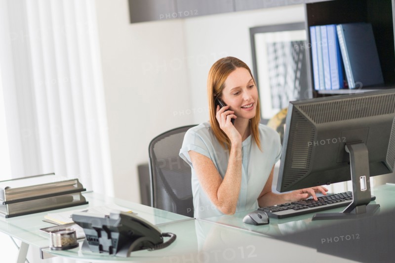 Business woman using computer and phone in office.