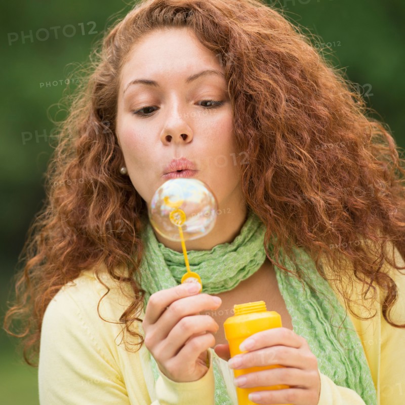 Young woman blowing bubbles in park.