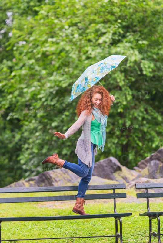Woman with umbrella dancing on bench in park.