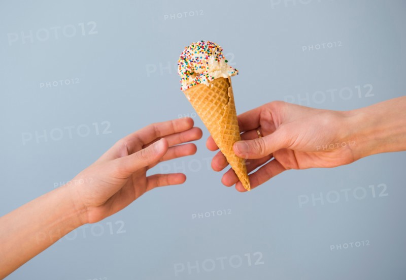 Hands passing ice cream against blue sky