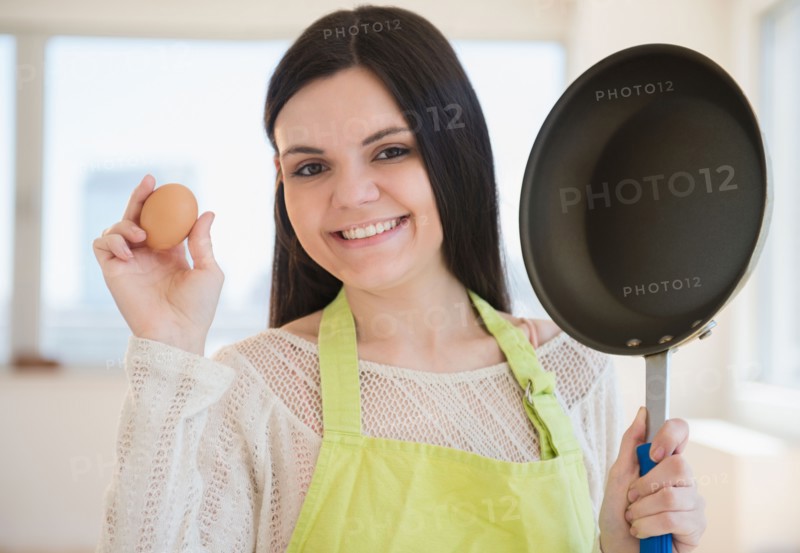 Young woman holding frying pan and egg