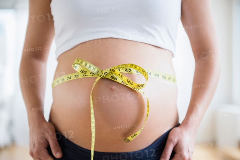 Mid section of pregnant woman with tape measure tied up on her belly