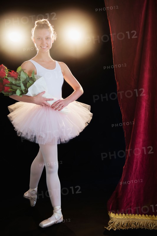 Teenage (16-17) ballerina on stage holding bunch of roses