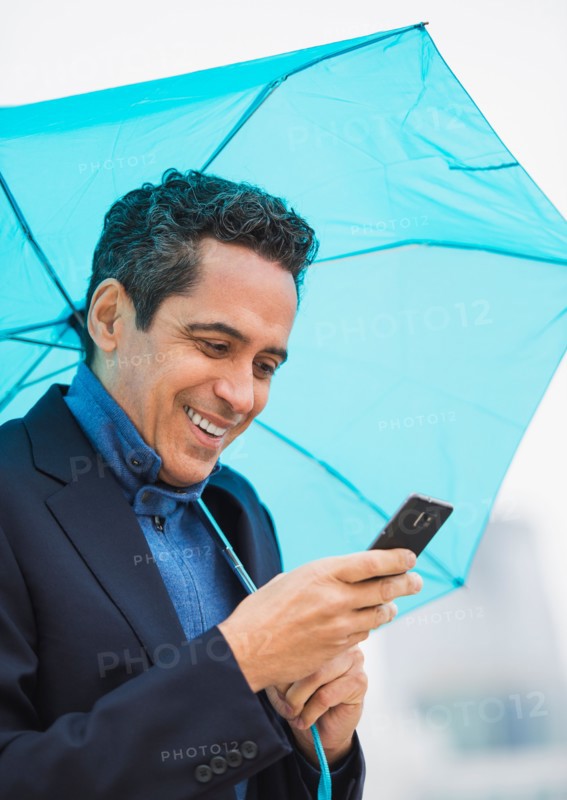 Portrait of man holding blue umbrella and using mobile phone