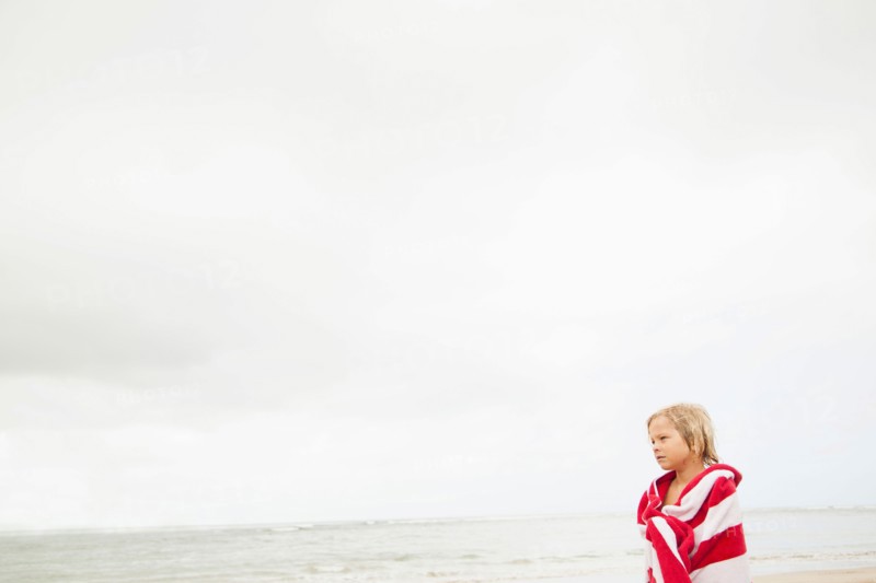 Boy (6-7) wrapped in towel on beach