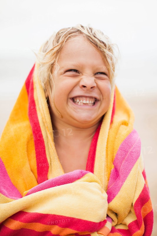 Boy (6-7) wrapped in towel on beach