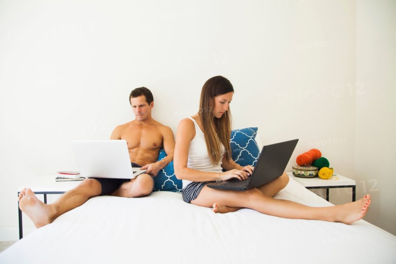 Couple lying on bed with laptops