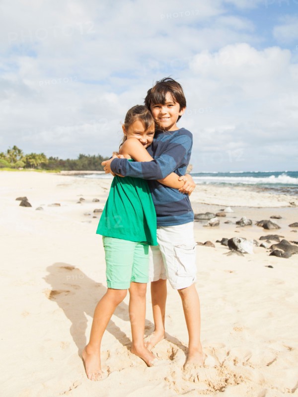 Portrait of girl (6-7) and boy (10-11) embracing on beach