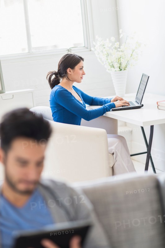Woman using laptop and man using digital tablet at home.