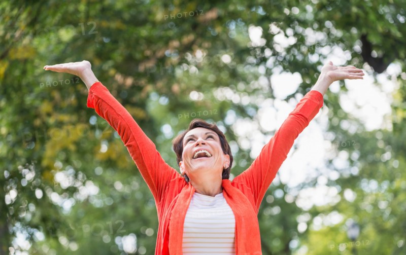Happy mature woman raising hands in park.