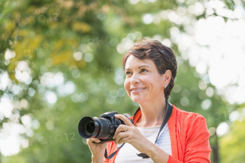 Mature woman holding camera in park.