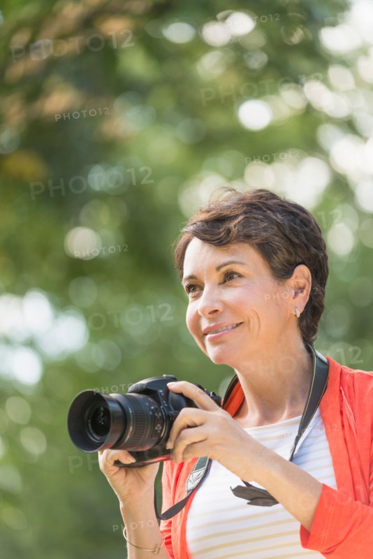 Mature woman holding camera in park.