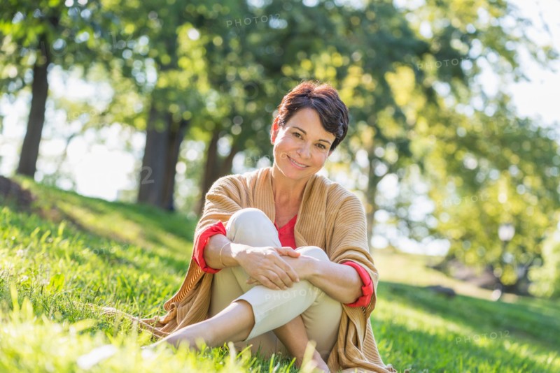 Mature woman sitting on grass in park.