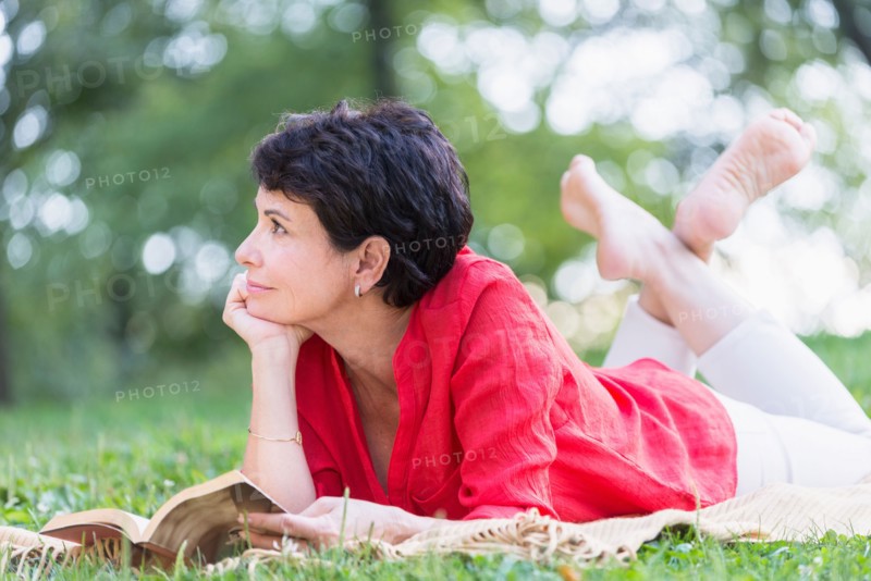Mature woman lying on grass and reading book.