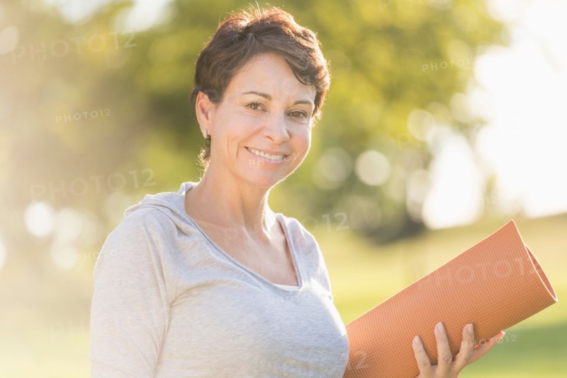 Mature woman holding yoga mat outdoors.