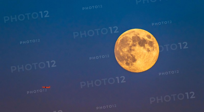 Plane flying across clear sky with full moon.