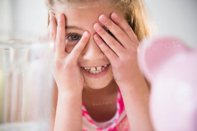 Girl (8-9) smiling and covering eyes