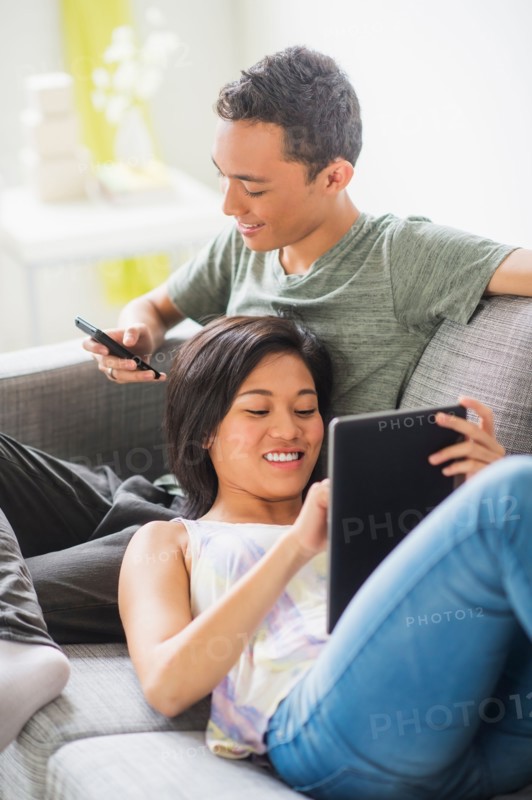 Young people using mobile phone and digital tablet on sofa