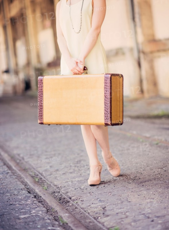 Low section of woman in dress holding suitcase at train station