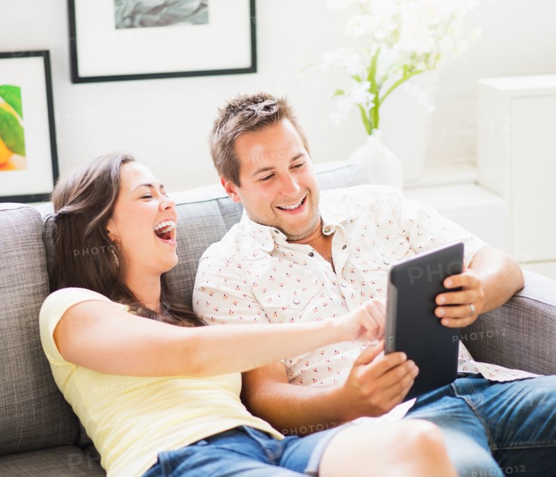 Portrait of playful couple using digital tablet on sofa