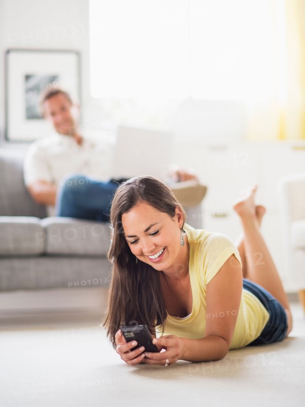 Woman lying on front and using mobile phone, man in background