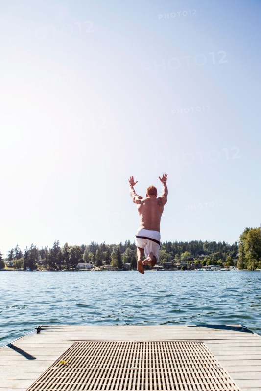 Young man jumping to lake from jetty